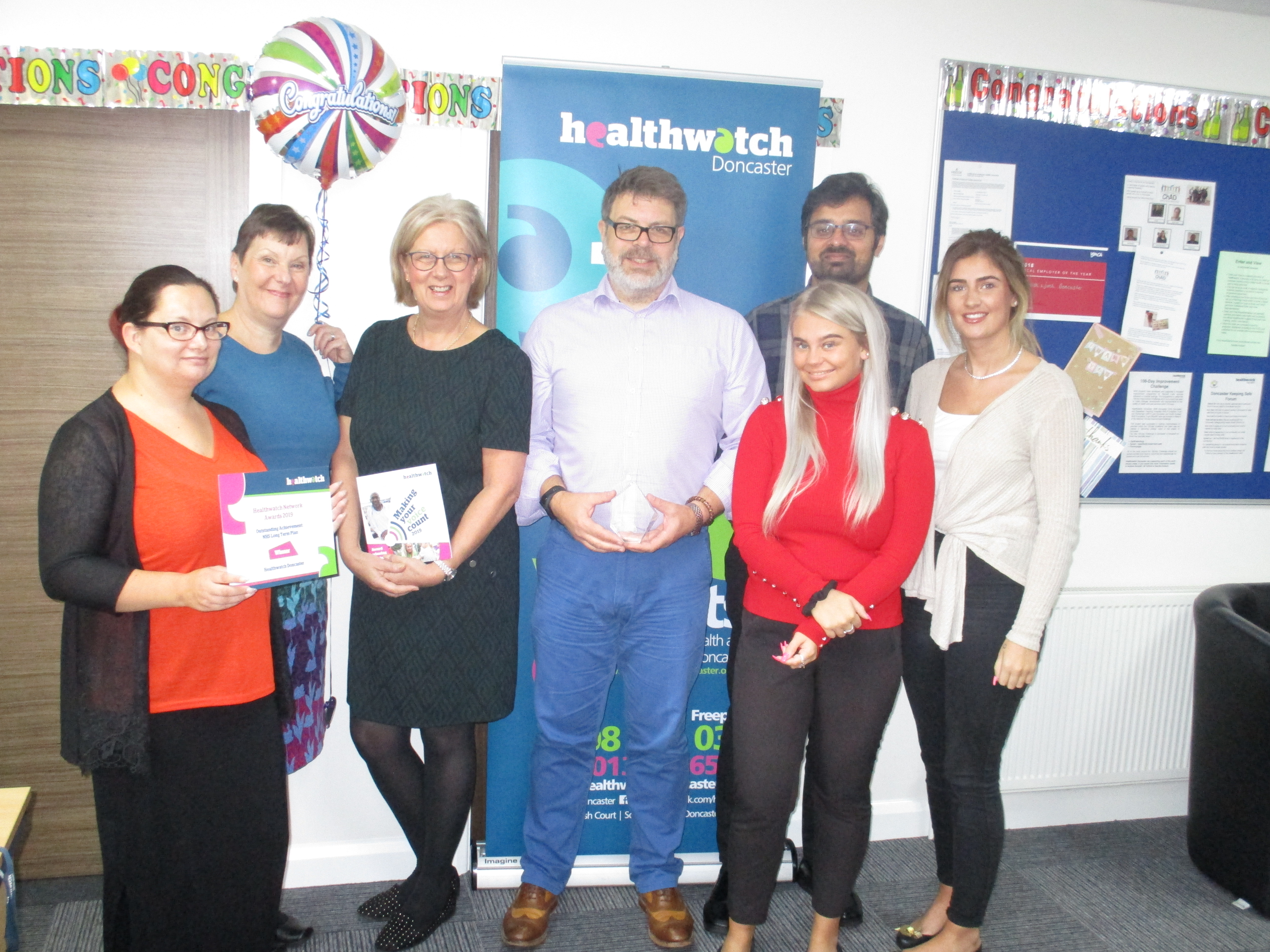 A group of people stood up smiling at the camera holding a trophy