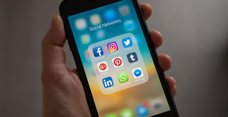 Someone holding a phone with applications in a folder, (Title: Social Networks. Includes: Facebook, Instagram, Twitter, Google+, Pinterest, Tumblr, LinkedIn, Whatsapp, Messenger.)
