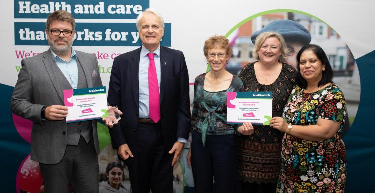 A group of people stood up smiling at the camera holding a certificate