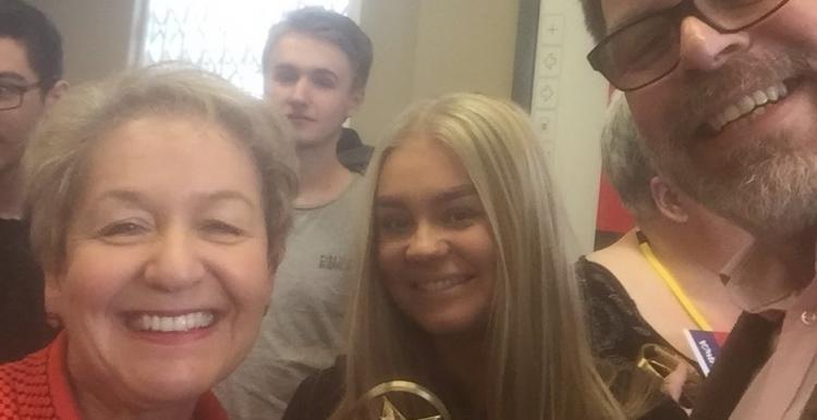 A group of people stood up smiling at the camera holding a trophy