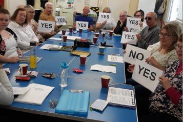 A group of volunteers sat around the table at a meeting holding up Yes or No signs
