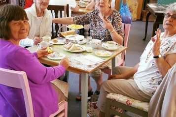 A group of older women sat around the table with cups of tea